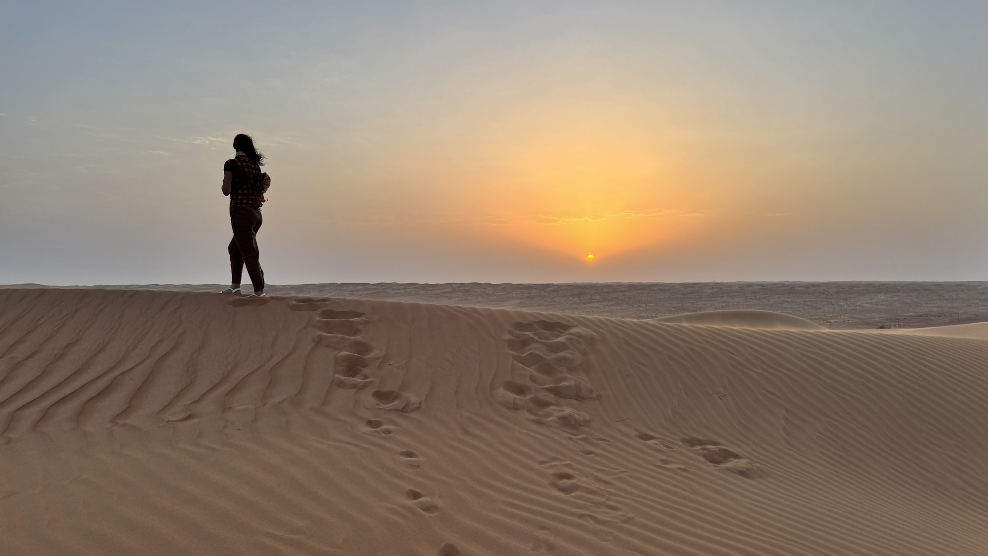 Traveler walking across desert dunes at sunset